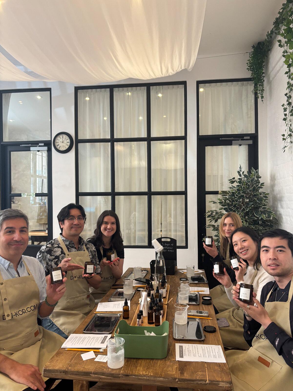 The team in aprons at a candle-making workshop, holding up their candles