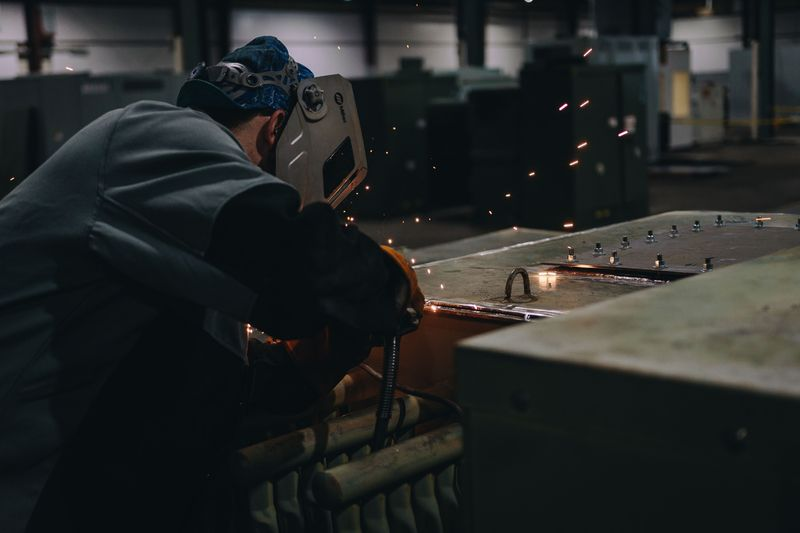 A welder working on a transformer housing in a workshop