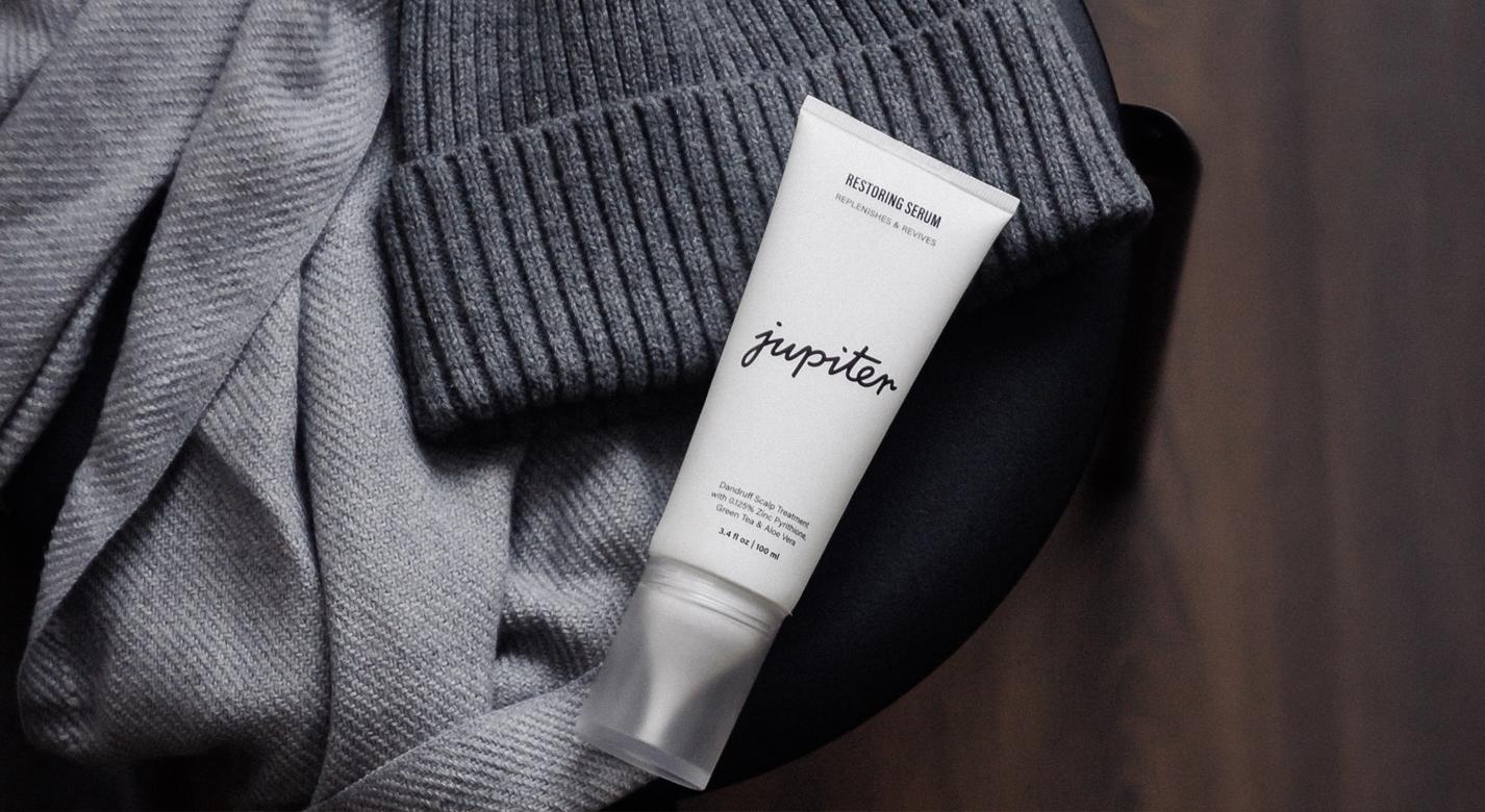 A tube of Jupiter Restoring Serum lying on a grey knit beanie and scarf