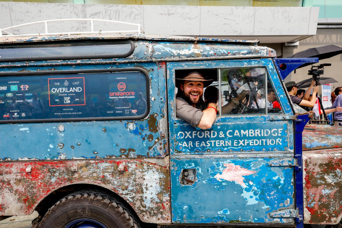 Smiling man leaning out of a weathered blue expedition vehicle