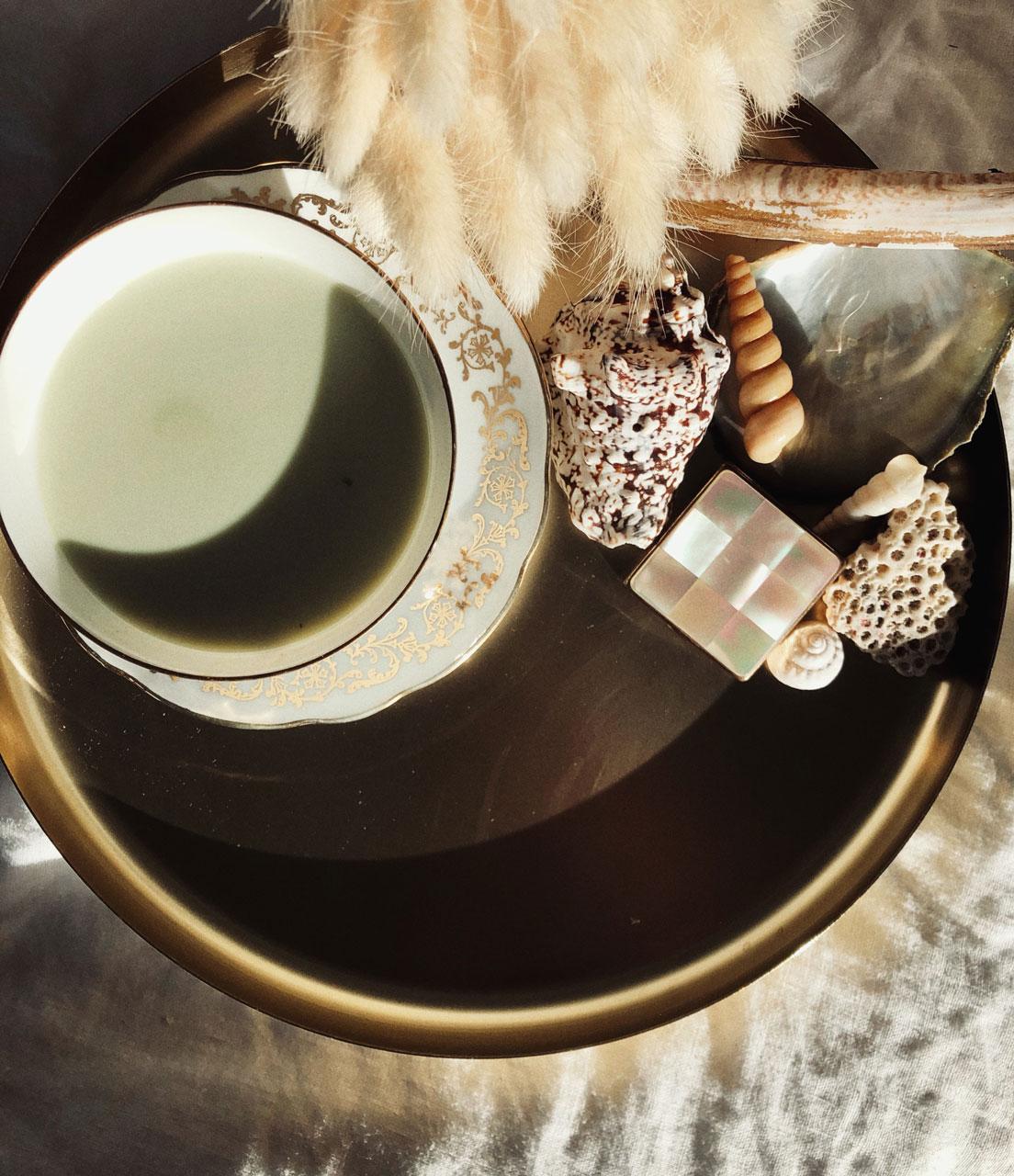 A cup of green drink on a tray with shells and dried flowers, from Apnée's brand photography