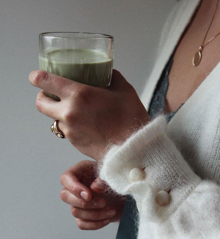 A woman in a white knit sweater holding a glass of green drink