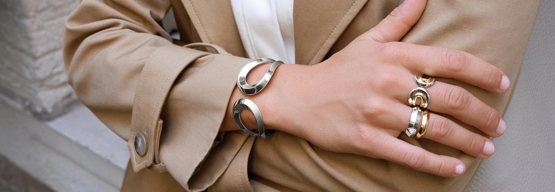 A model in a trench coat wearing CAST silver and gold cuffs and stacked rings