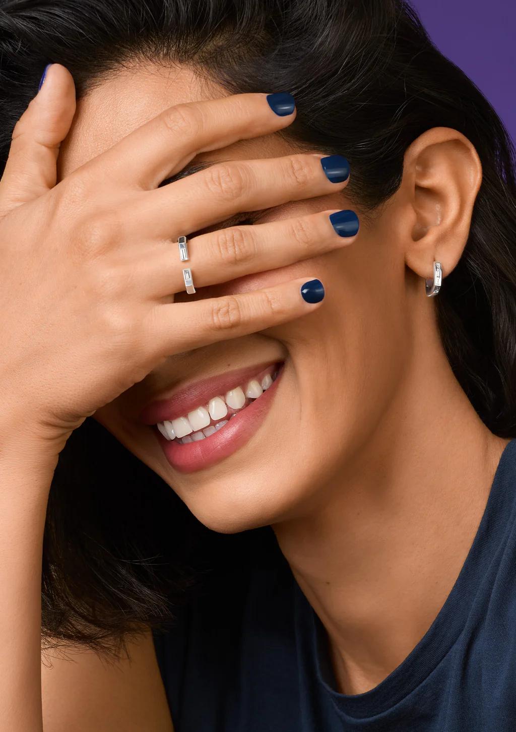 A smiling model wearing CAST silver rings and huggie earrings