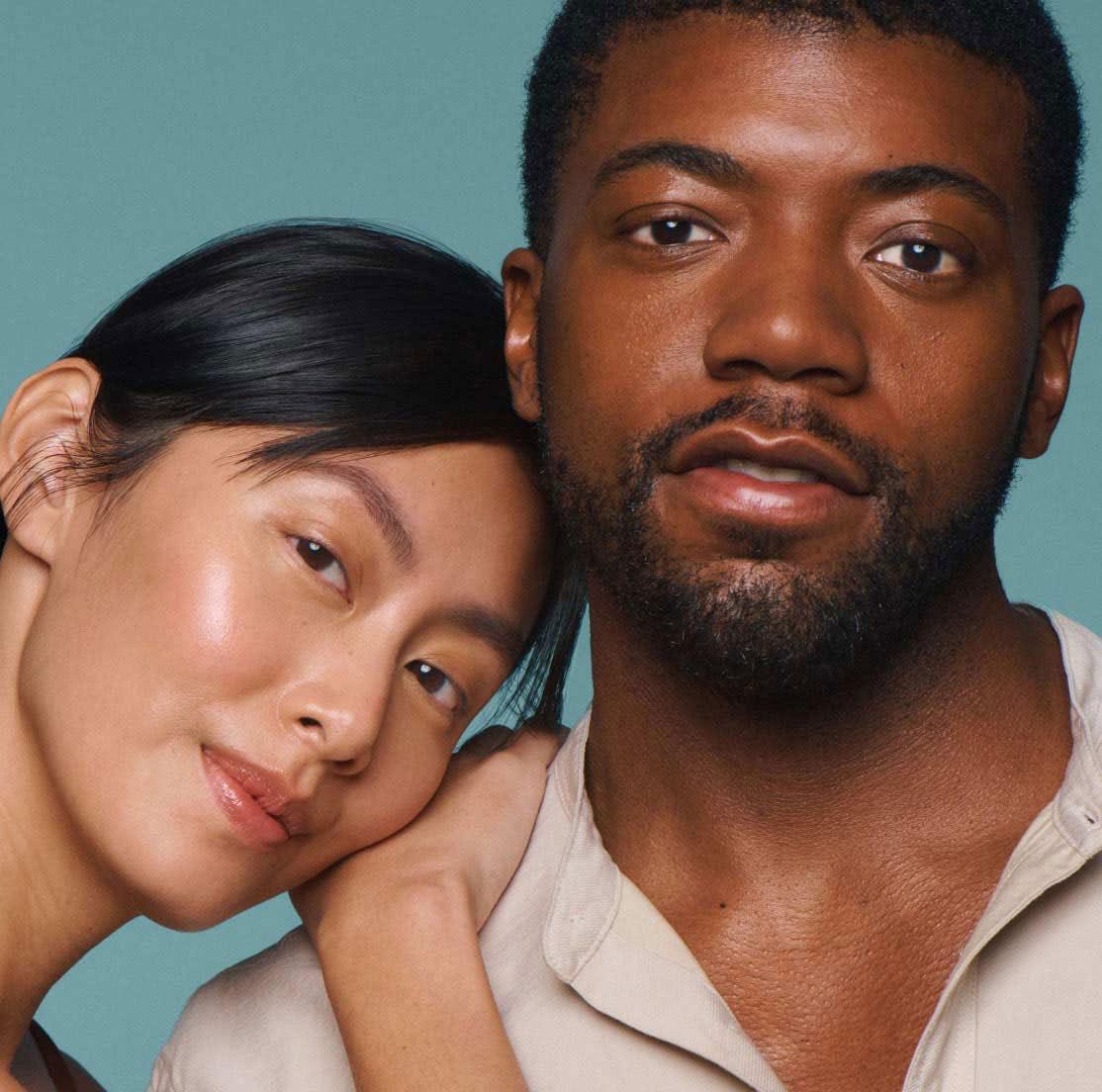 Two models posing cheek to cheek against a teal backdrop