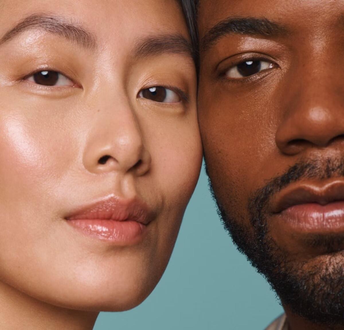 Close-up of two models' faces, cheek to cheek, against a teal backdrop