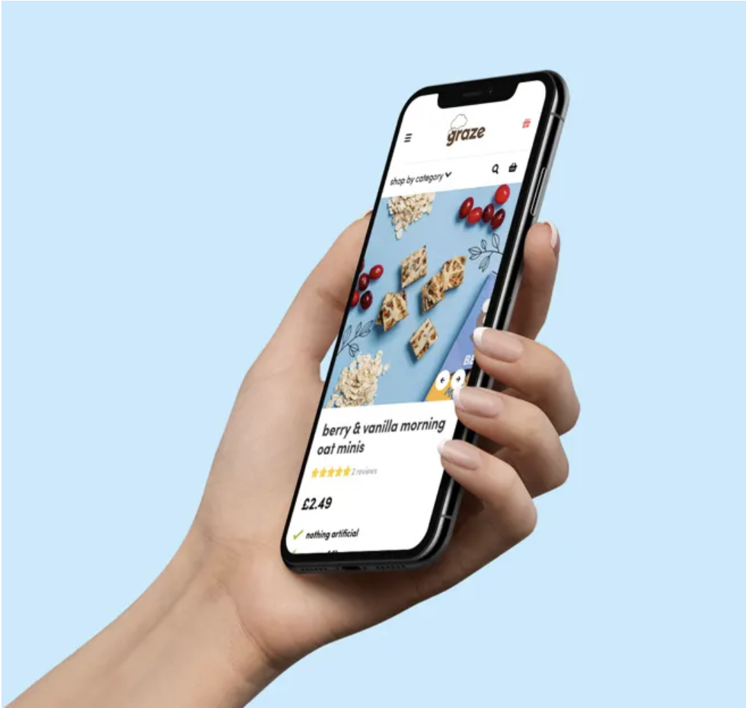 A hand holding a phone showing a Graze product page for berry and vanilla oat minis