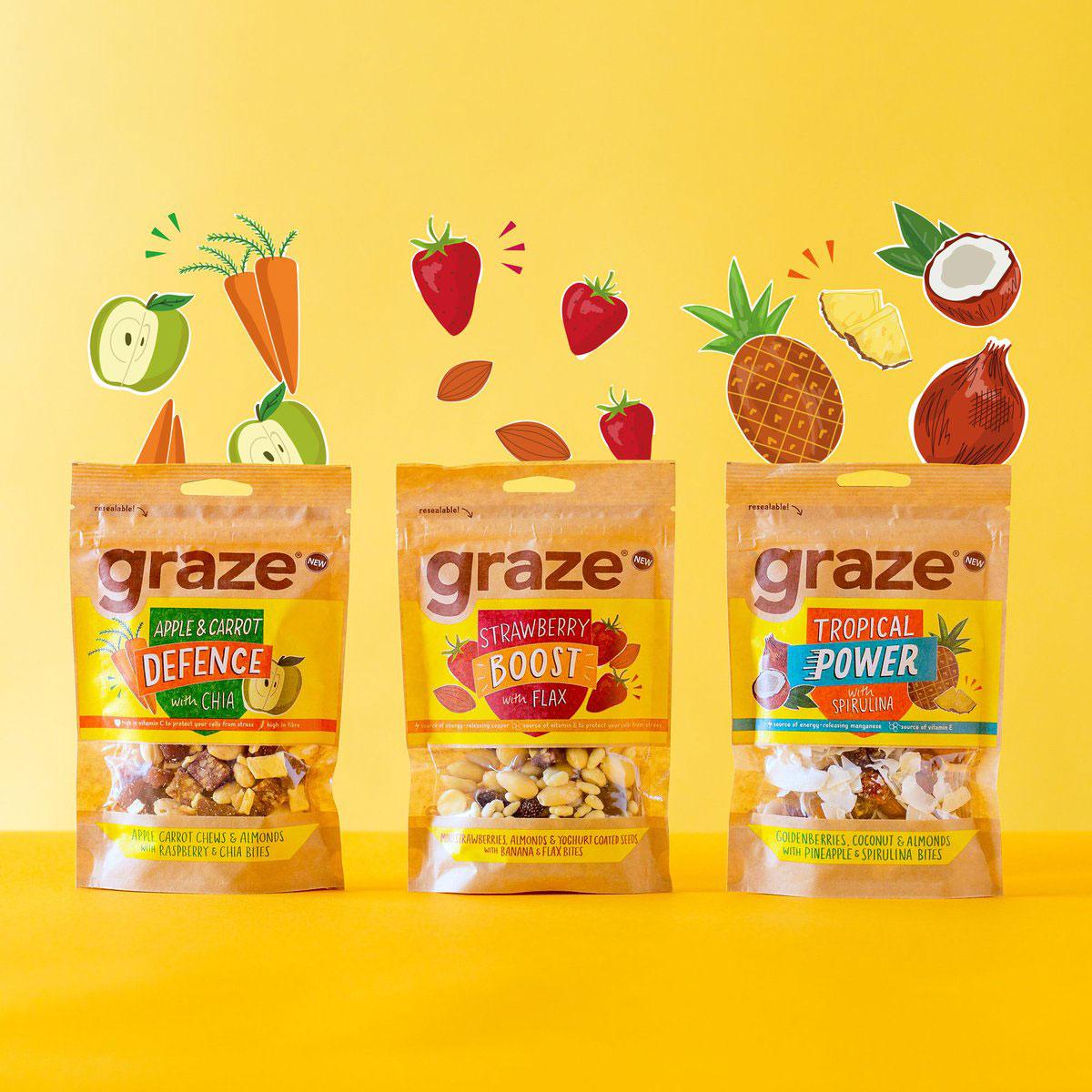 Three Graze snack bags falling among fruit and vegetables on a yellow background