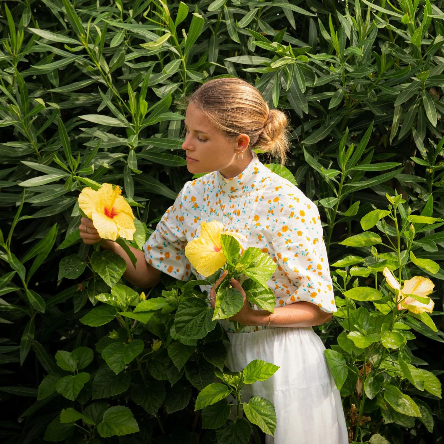 A woman in a floral shirt picking yellow hibiscus flowers