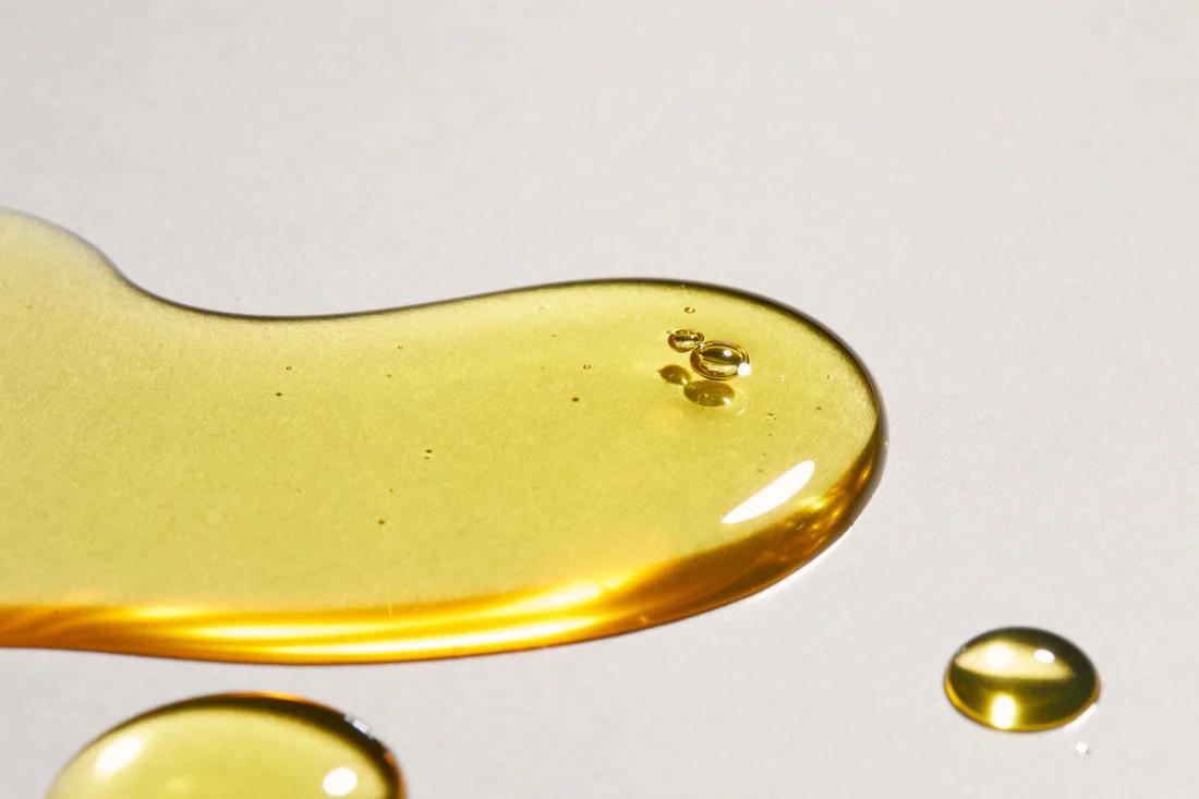 A drop of golden facial oil on a white surface