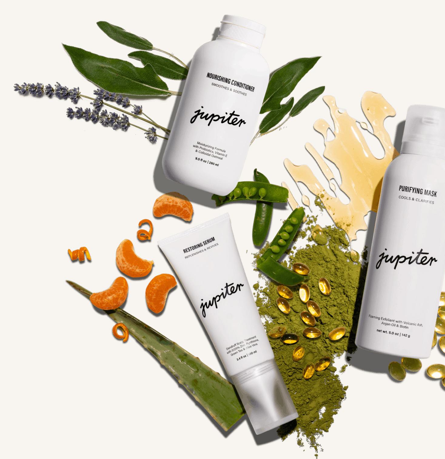 Three Jupiter haircare products arranged in a flat lay with the botanical ingredients they are made from