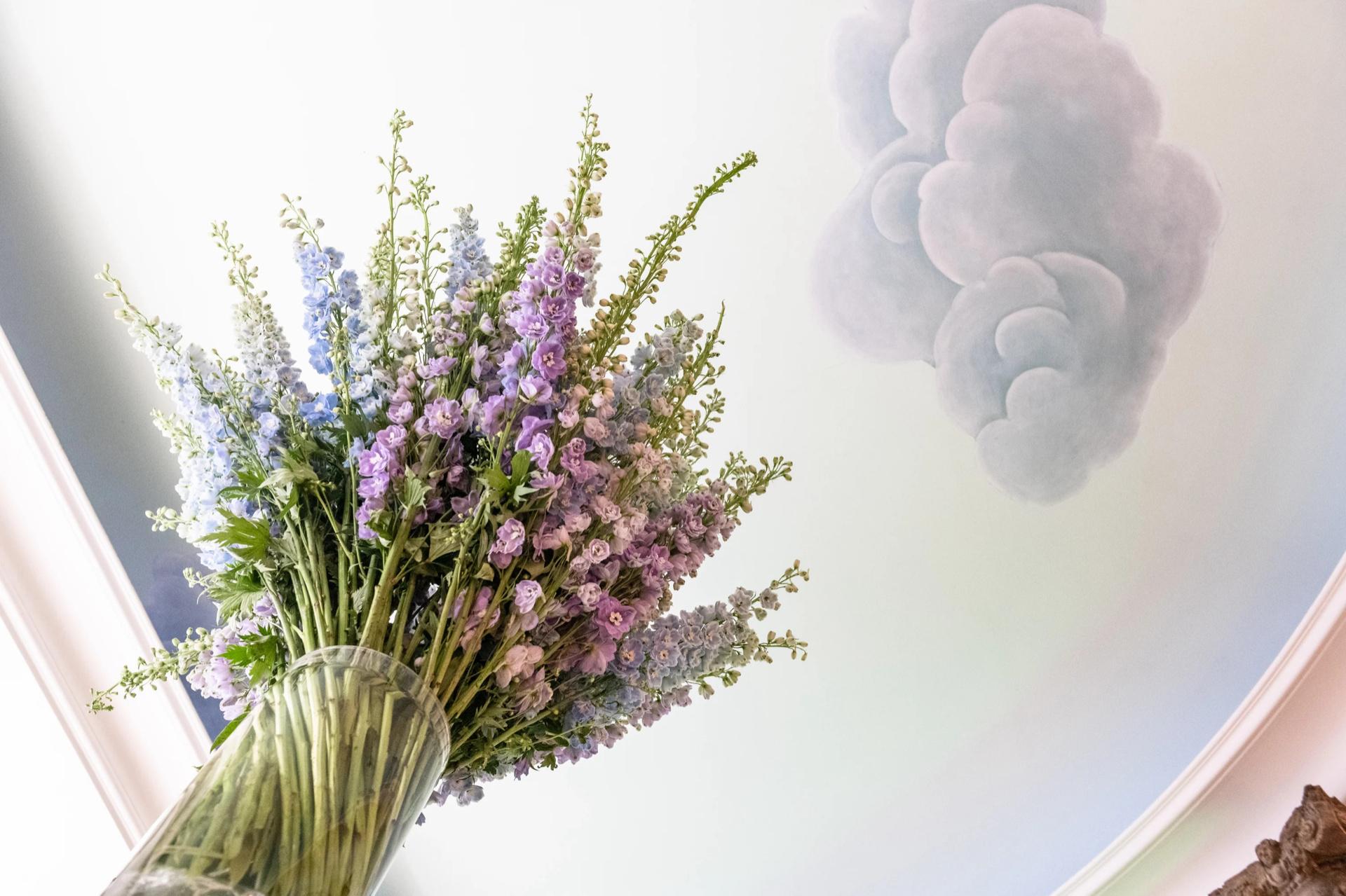 A purple and pink Lachaume bouquet in a vase against a painted sky